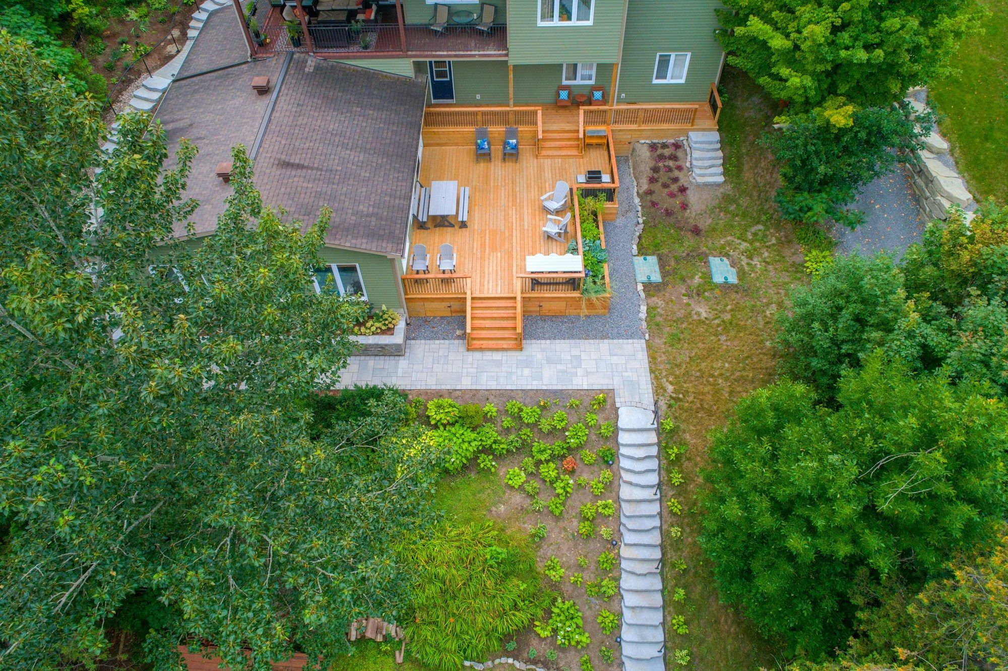 Vue de dessus d’une maison avec terrasse en bois et jardin arboré